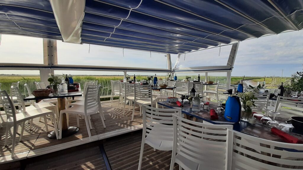 Terrasse de restaurant ombragée avec chaises blanches et vue panoramique sur les marais verdoyants.