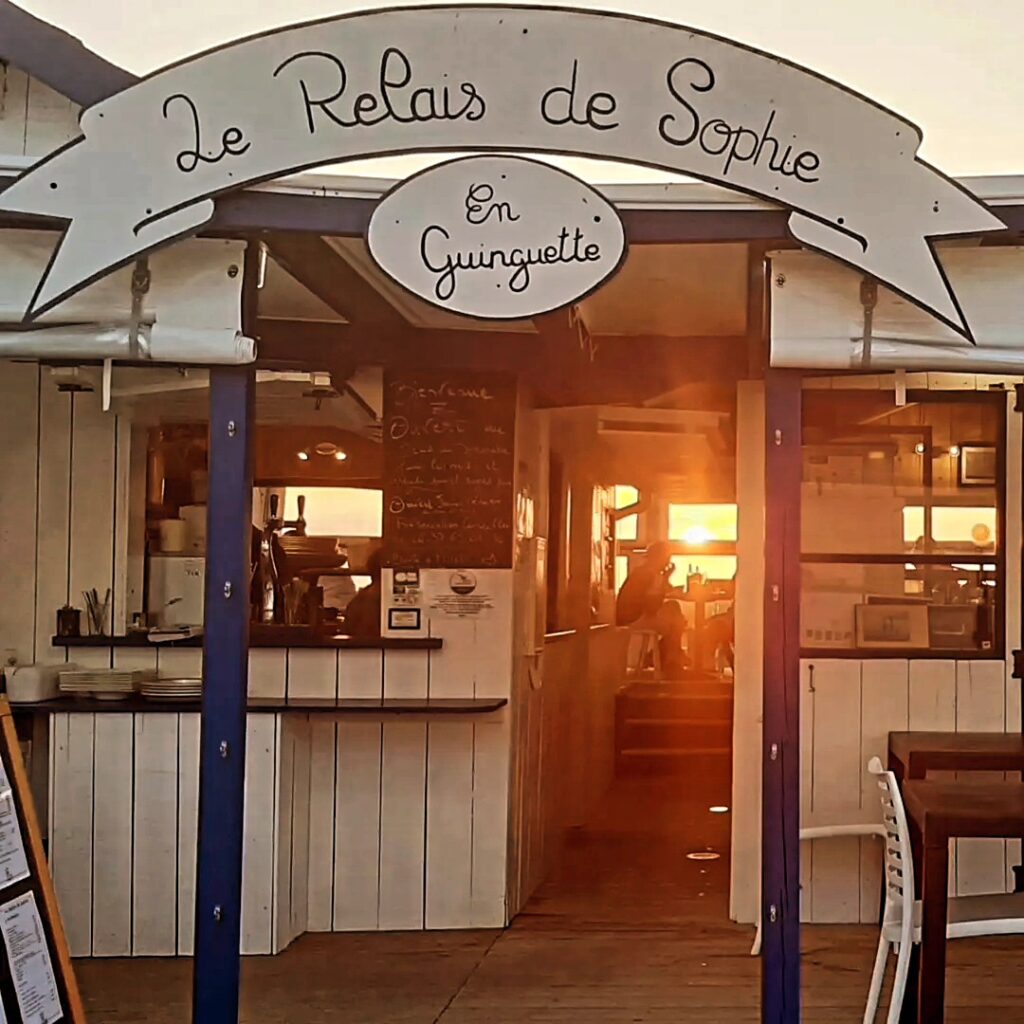 Le Relais de Sophie En Guinguette : entrée en bois rustique illuminée par un coucher de soleil chaleureux.